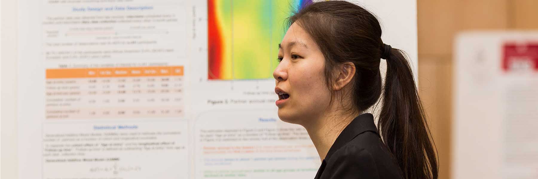 A woman speaks in front of charts and graphs.